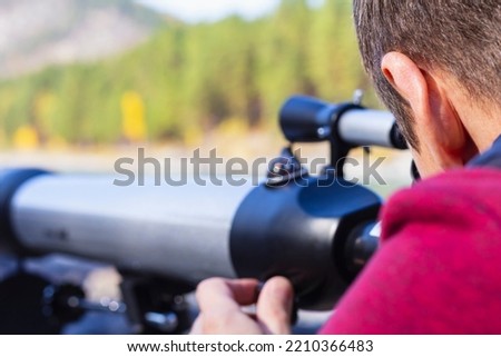 Focus on man's head looking at mountain peaks in telescope on valley of mountain river, selective focus. Optical telescope, out of focus, device instrument for planetary observation of distant object Royalty-Free Stock Photo #2210366483