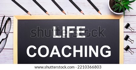 On a light wooden table - a board with the text LIFE COACHING, pencils, plants, glasses and paper clips. Business concept