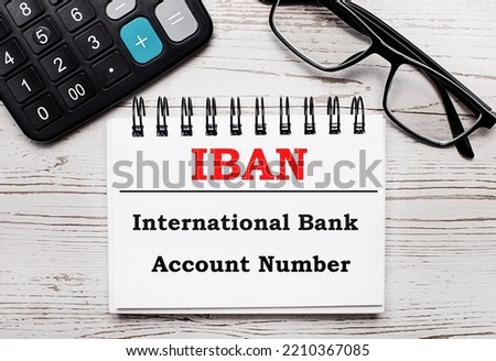 On a light wooden table calculator, glasses and a blank notepad with the text IBAN International Bank Account Number. Business concept