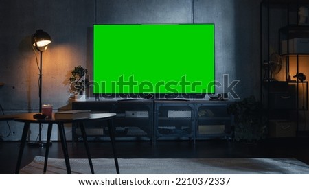 Stylish Loft Apartment Interior with TV Set with Green Screen Mock Up Display Standing on Television Stand. Empty Cozy Living Room of Spacious Flat with Chroma Key Placeholder on Monitor. Royalty-Free Stock Photo #2210372337