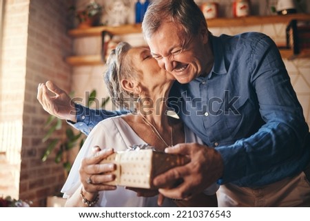 Elderly, couple and happy with gift, surprise and kiss on face together in home. Man, woman and retirement show love, romance and happiness giving present for anniversary, birthday or mothers day