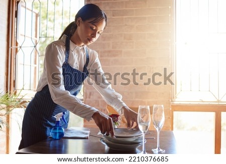 Restaurant waitress cleaning dishes from table after a meal. Customer service, diner and working in the food industry as a waiter clearing dirty plates, glasses and leftovers to clean dinner table Royalty-Free Stock Photo #2210376685