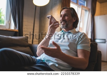 Bearded man sitting in the armchair awith a smartphone in hand Royalty-Free Stock Photo #2210378339