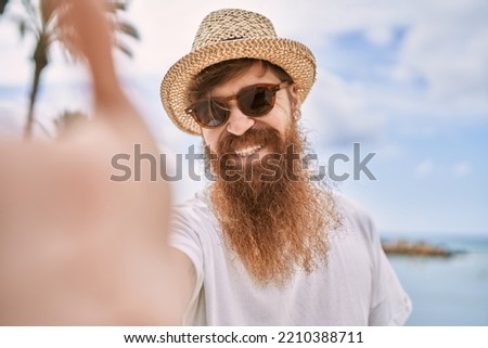 Young redhead tourist man smiling happy make selfie by the camera at the beach.