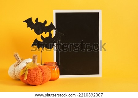 mocap black plate and halloween decor on a bright yellow background, candle, felt bats, knitted and fabric homemade pumpkins for holiday decoration, space for text, advertising, invitations