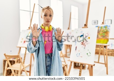 Young caucasian girl at art studio moving away hands palms showing refusal and denial with afraid and disgusting expression. stop and forbidden. 