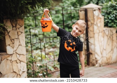 Kid boy teenager holding jack-o-lantern pumpkin bucket with candies and sweets. Kid trick or treating in Halloween holiday. Royalty-Free Stock Photo #2210428733