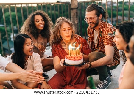 A birthday girl blows candles and wishes a wish while her friends look at her. A man holds a birthday cake while a girl blows the candles. The rest of the crew smiles and looks at her. Royalty-Free Stock Photo #2210431737
