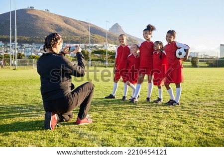 Soccer, phone and team picture with coach, ball and sports girl group with a smile together on a field. Young female football squad happy with post for social media on a sports ground after training