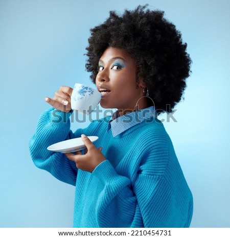 Afro hair, tea cup and black woman with fashion, style and trend clothes on blue background in studio with bold makeup cosmetics. Portrait, gossip and beauty model with wow or surprise face and drink Royalty-Free Stock Photo #2210454731