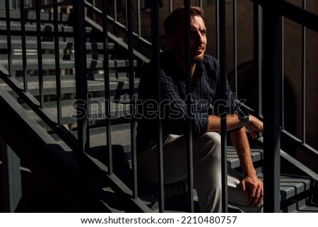 a guy in a shirt and light trousers is sitting on the iron stairs
