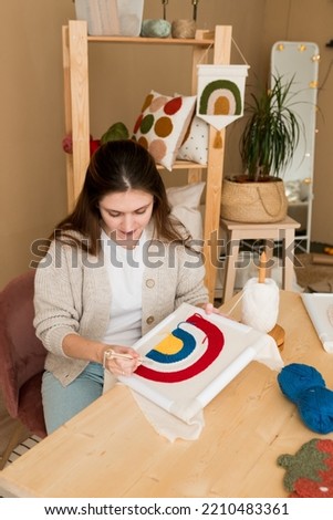 Modern punch needle kit for beginners. Young woman embroidering handmade picture rainbow on canvas in workshop. Handicraft, hobby, diy for decoration home concept Royalty-Free Stock Photo #2210483361