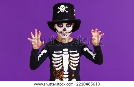 Happy cheerful boy in skeleton costume celebrates Halloween and make scary gesture on  bright purple background