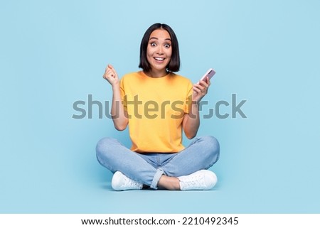 Full body size photo of young chinese cute girl hold new smartphone happy buy new app for work excited fist up celebrate isolated on blue color background