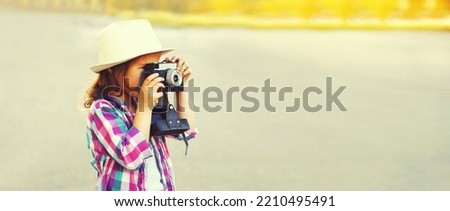 Portrait of child with film camera taking picture wearing summer straw hat on the city street