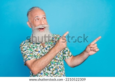 Photo of funny dreamy man pensioner dressed flower print shirt pointing two fingers looking empty space isolated blue color background