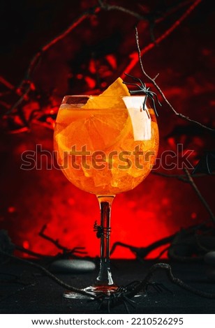 Halloween aperol spritz cocktail on scary dark bloody red background with twisted branches, bats, stones and spiders,  festive drink for party