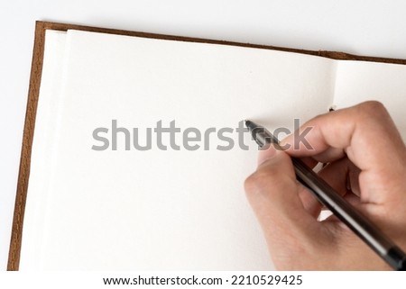 Writing in blank notepad, man hand with pen next to an empty blank notepad taking notes concept