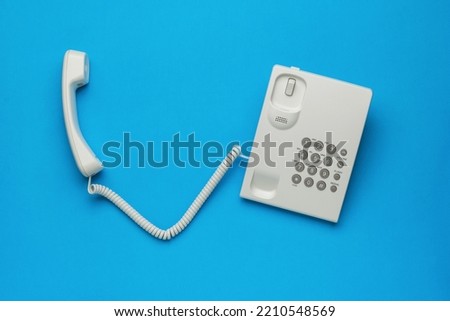 A white telephone with the receiver off on a blue background. The concept of telephone communication. Flat lay.
