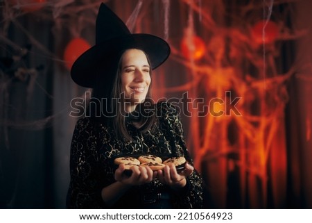 
Happy Woman Dressed in Witch Costume Holding Halloween Cookies. Cheerful Party Host Holding a Plate of Biscuits 
