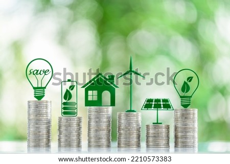 Renewable or clean energy generation prices and costs, financial concept : Green eco-friendly symbols atop coin stacks e.g. energy efficient light bulb, a battery, a solar cell panel, a wind turbine. Royalty-Free Stock Photo #2210573383