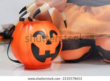 A child in a Halloween costume and claws sits next to a candy bucket