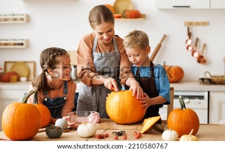 Happy kids boy and girl helping mother to carve Halloween pumpkin while standing in kitchen at home and preparing for autumn holiday, family children and mom making Jack-o-Lantern together