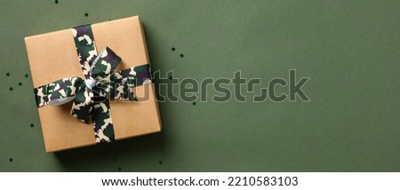 Gift box with camouflage military ribbon bow and confetti stars on green background. Veterans Day banner design.