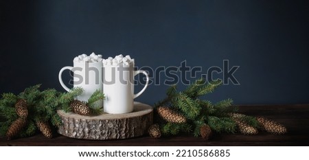 two white cups with drinks with marshmallows and christmas decorations on dark background