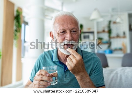 Senior man takes pill with glass of water in hand. Stressed mature man drinking sedated antidepressant meds. Man feels depressed, taking drugs. Medicines at work Royalty-Free Stock Photo #2210589347