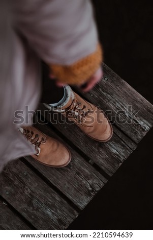 Woman in boots standing on a wooden pier. Female in brown boots reaching by her hand to a wooden pier in lake area.