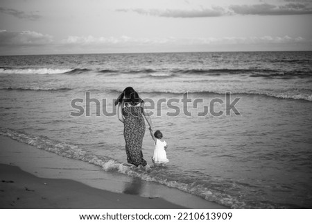 Mom and daughter walking on the beach black and white