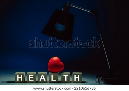 Wooden cubes with the inscription HEALTH on a table in total darkness and the glow of a table lamp illuminating a red heart