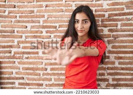 Young teenager girl standing over bricks wall rejection expression crossing arms and palms doing negative sign, angry face 
