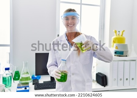Young blonde woman wearing scientist uniform measuring liquid at laboratory