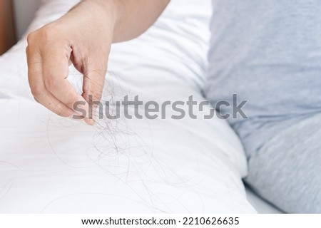 closeup hand holding hair loss fallen on pillow 