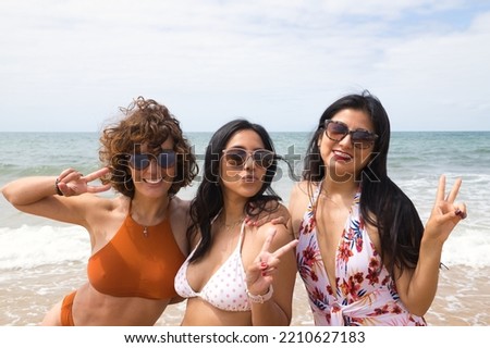 Attractive mature woman next to two young, pretty, brunette South American women in bikinis and sunglasses taking funny pictures of each other. Concept vacation, friends, multiethnic, summer.