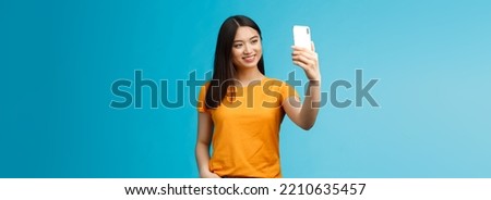 Stylish good-looking asian cute girl hold smartphone talking video-call smiling broadly look phone screen, taking selfie, feeling pretty, talking followers online social media, blue background