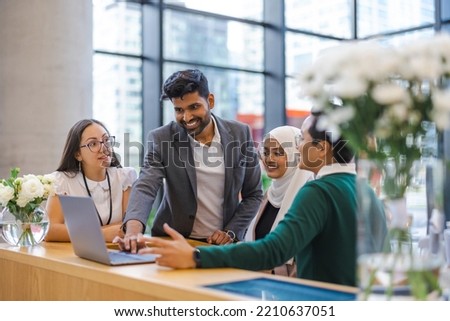 A diverse group of business people gather around a laptop in a modern office
