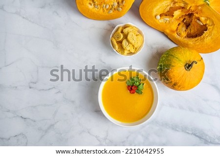 Autumn pumpkin cream soup with pumpkin spices. Delicious and bright vegetarian dish with foodstyling of fresh parsley with hot pepper and seasonings on a white background. Flatlay with copy space text