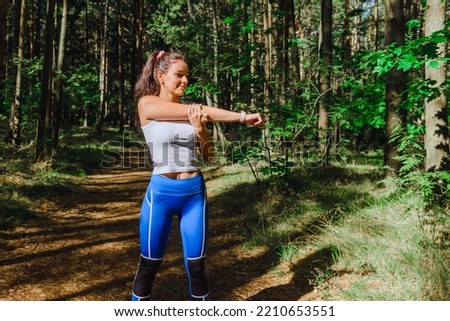 Young pretty Woman stretching arms and breathing fresh air in a summer forest while exercising. Workouts and Lifestyles concept. Healthy life and Healthcare theme.Nature and Outdoors concept.
