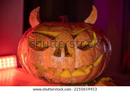on the table there is a carved Halloween pumpkin with horns and a red backlight on the background