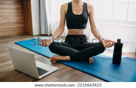 A sporty woman in sportswear is sitting on the floor with dumbbells and a protein shake or a bottle of water and is using a laptop. Sport concept.