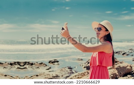 Young woman on vacation taking photos on the beach, Smiling girl in hat taking photos on the beach. Beach vacation concept. Girl in hat on the beach taking a selfie