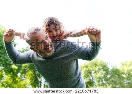 Father giving a daughter piggyback ride when playing in the park. Royalty-Free Stock Photo #2210671785