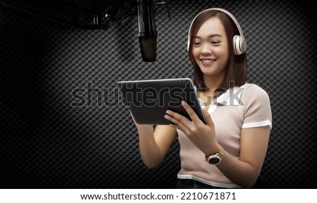 Asian women voice their voices or record annoucement a song in the sound studio with a microphone and a script on the tablet