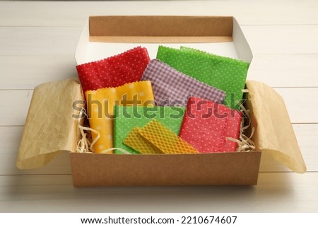 Colorful beeswax food wraps in box on white wooden table Royalty-Free Stock Photo #2210674607