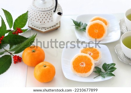 New year japanese  dessert,  mandarin orange daifuku on white  pltaes with cups of green tea