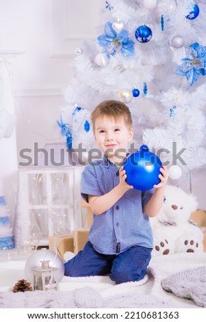 Cute boy in a blue shirt near a white Christmas tree  in a room decorated for Christmas. Family Christmas. Christmas mood
