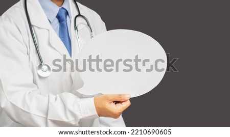 Midsection of a doctor in uniform holding a blank speech bubble while standing on a gray background. Space for text. Healthcare and advertising concept